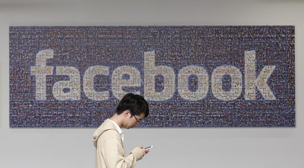 FILE - In this June 11, 2014 photo, a man walks past a Facebook sign in an office on the Facebook campus in Menlo Park, Calif. Facebookís recent effort to force people to adopt its standalone mobile messaging app has privacy-concerned users up in arms. In truth, Facebook Messenger isnít any more invasive than Facebookís main app _or other similar applications. (AP Photo/Jeff Chiu, File)