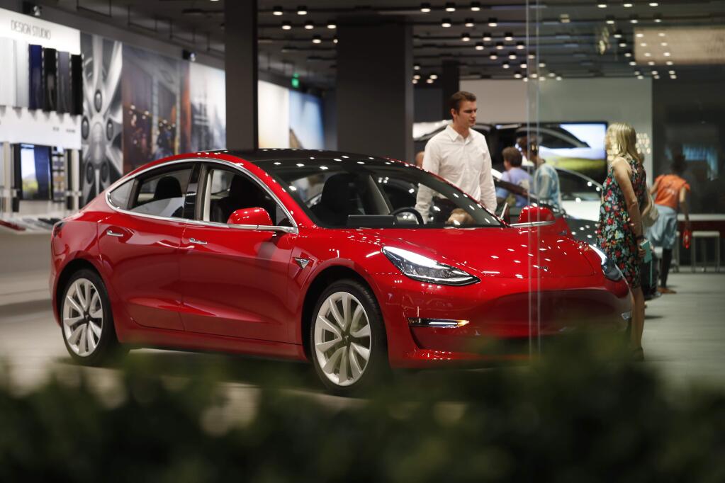 FILE- In this July 6, 2018, file photo, a prospective customer confer with sales associate as a Model 3 sits on display in a Tesla showroom in the Cherry Creek Mall in Denver. On Tuesday, Jan. 1, 2019, the federal credit for Tesla buyers dropped from $7,500 to $3,750. It will gradually be phased out this year. (AP Photo/David Zalubowski, File)