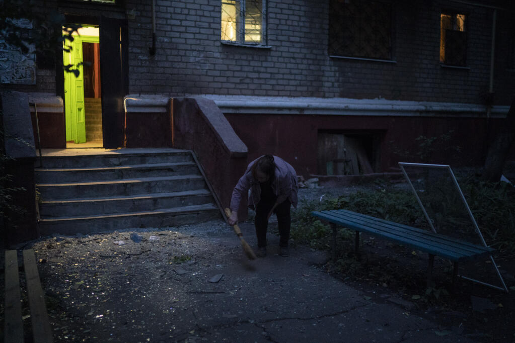 A woman cleans up shattered glass from the entrance of a residential building that was damaged after a Russian attack in Kramatorsk, Ukraine, Monday, Sept. 26, 2022. (AP Photo/Leo Correa)