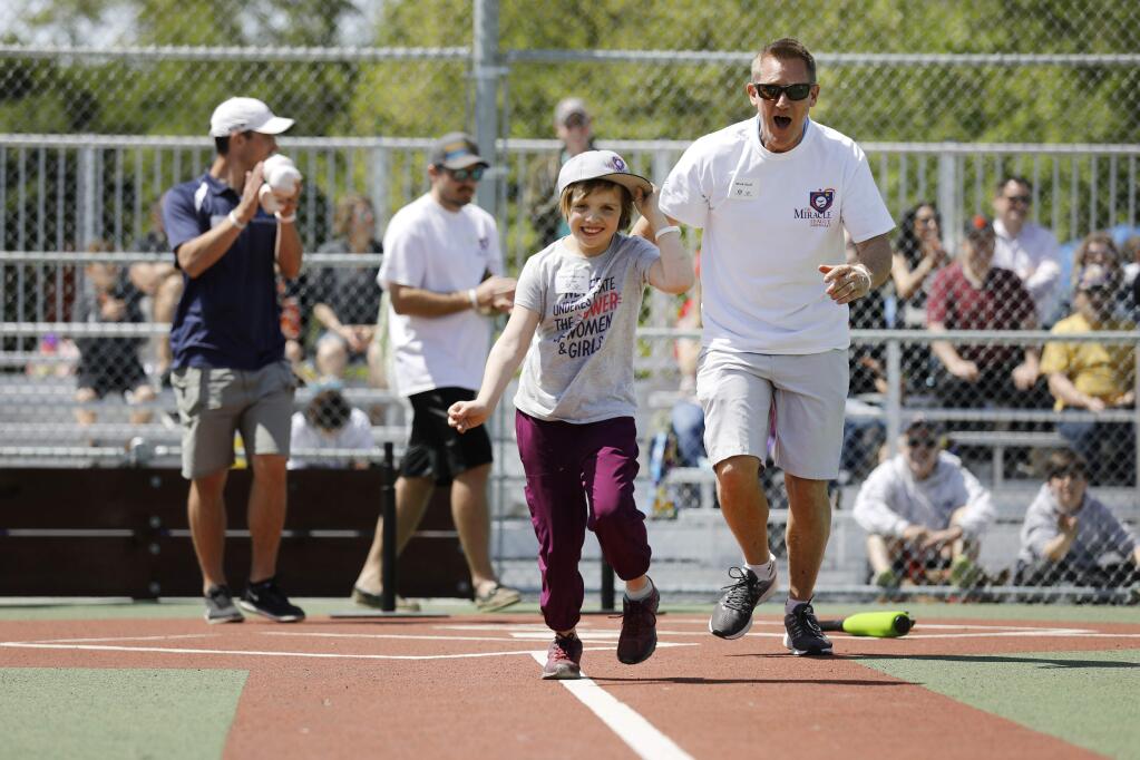 Violet Albrecht-Brown, 8, is cheered on by volunteer Mark Wolf as she runs towards first base after hitting the ball during the opening day celebration of the Miracle League field at Lucchesi Park in Petaluma, California on Sunday, April 14, 2019. (BETH SCHLANKER/The Press Democrat)