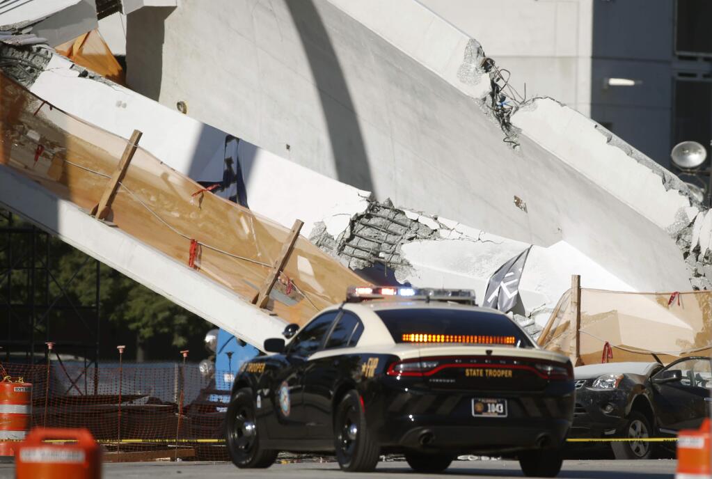 A Florida Highway Patrol vehicle is parked next to a crushed car under a section of a new pedestrian bridge, Friday, March 16, 2018, after it collapsed Thursday onto a highway at a Miami-area college. Authorities said the bridge being built at Florida International University had been put to a 'stress test' and its cables were being tightened when it collapsed. (AP Photo/Wilfredo Lee)