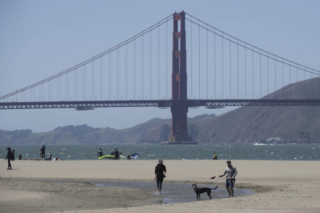 People walk on the sand in front of the Golden Gate Bridge at Crissy Field East Beach in San Francisco, Sunday, May 3, 2020, during the coronavirus outbreak.  (Jeff Chiu / Associated Press)