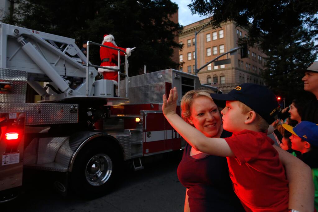 Banyan Parker holds her son Zakary, 4, as he waves to Santa Claus who arrives aboard Santa Rosa Fire Department's Truck 1 at Old Courthouse Square during Winterlights in Santa Rosa, California on Friday, November 24, 2017. (Alvin Jornada / The Press Democrat)