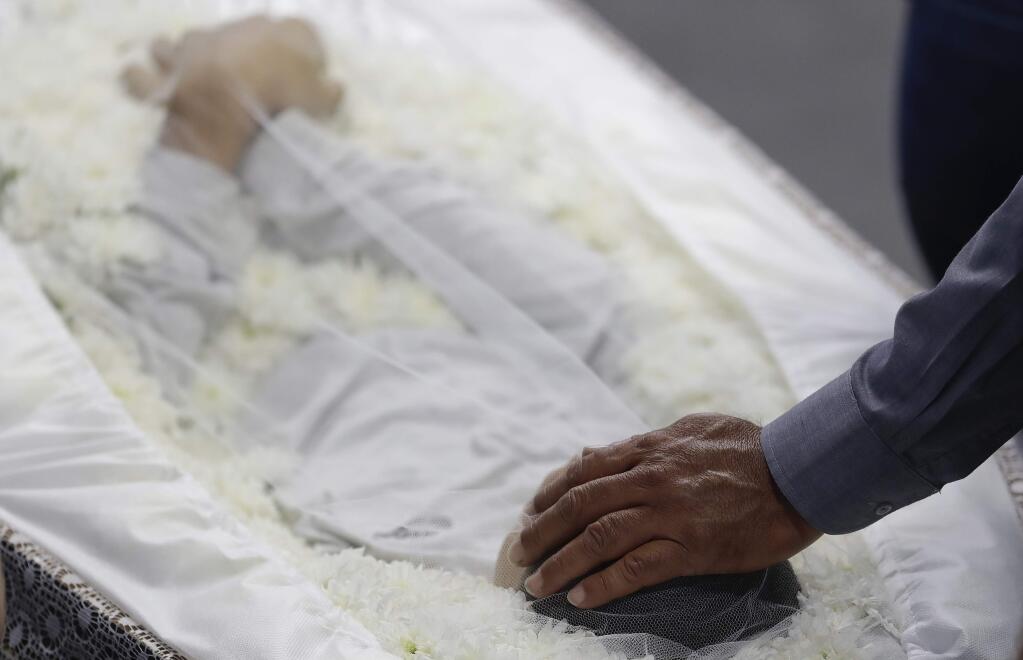 A relative places his hand on the head of school shooting victim Caio Oliveira during a collective wake for those who died in Suzano, greater Sao Paulo area, Brazil, Thursday, March 14, 2019. The Sao Paulo suburb prepares to bury its dead and look for reasons why two masked former students of the Raul Brasil state school, armed with a hand gun, knives, axes and crossbows killed five teenagers and two adults at a school before killing themselves as police closed in. (AP Photo/Andre Penner)