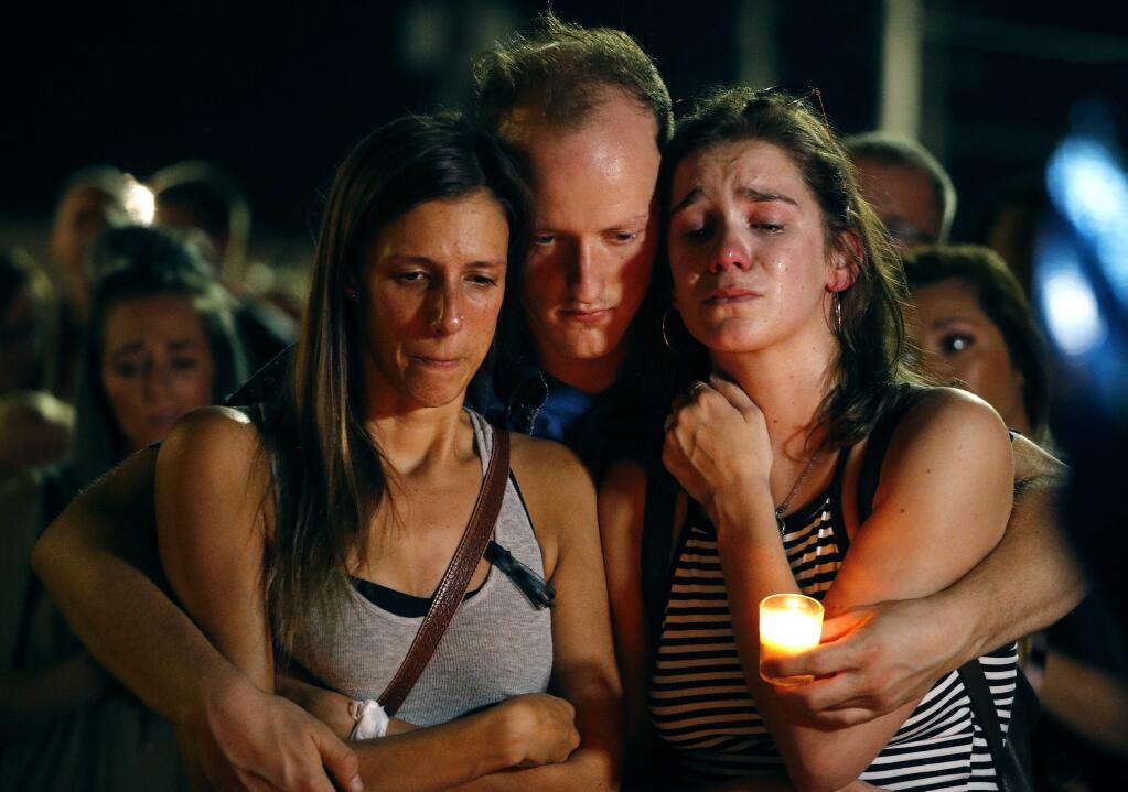 Mallory Cunningham, left, Santino Tomasetti, center, and Aubrey Reece attend a candlelight vigil in the parking lot of Ride the Ducks Friday, July 20, 2018, in Branson, Mo. One of the company's duck boats capsized Thursday night resulting in over a dozen deaths on Table Rock Lake. (AP Photo/Charlie Riedel)