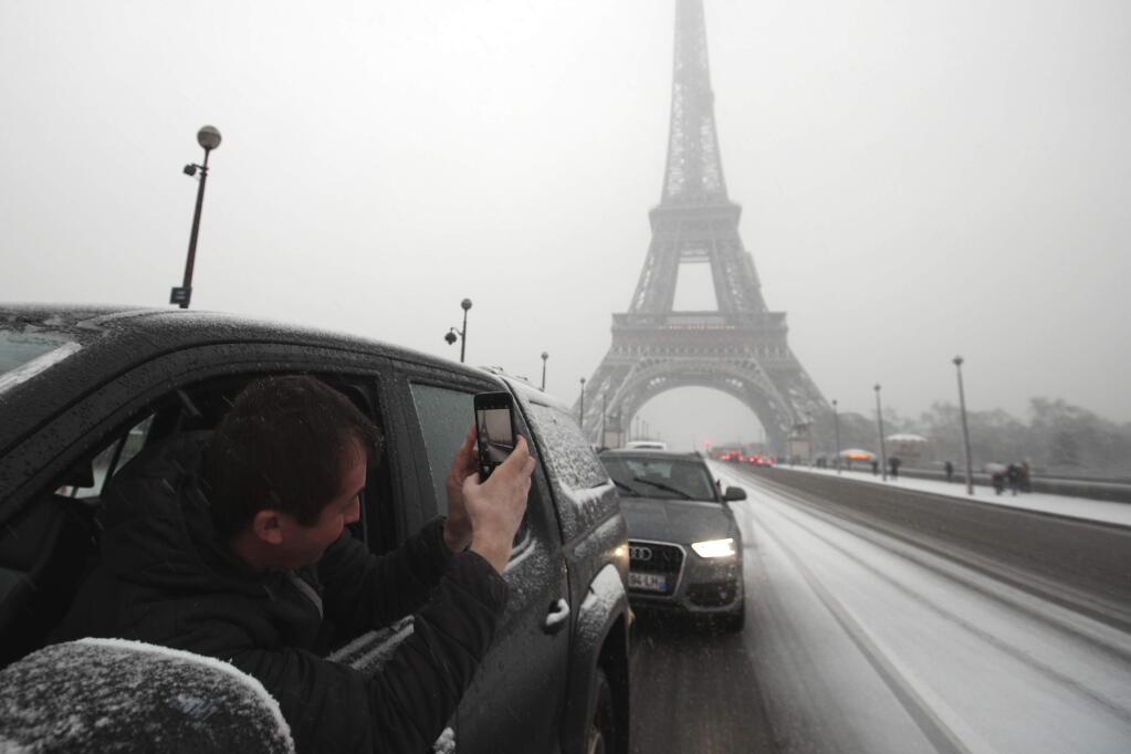 A driver takes a snapshot of the Eiffel Tower during first snowfall of the winter season in Paris, France, Tuesday, Feb. 6, 2018. France's national weather agency Meteo France said Tuesday about half the country is on alert for dangerous levels of snow and ice. (AP Photo/Francois Mori)