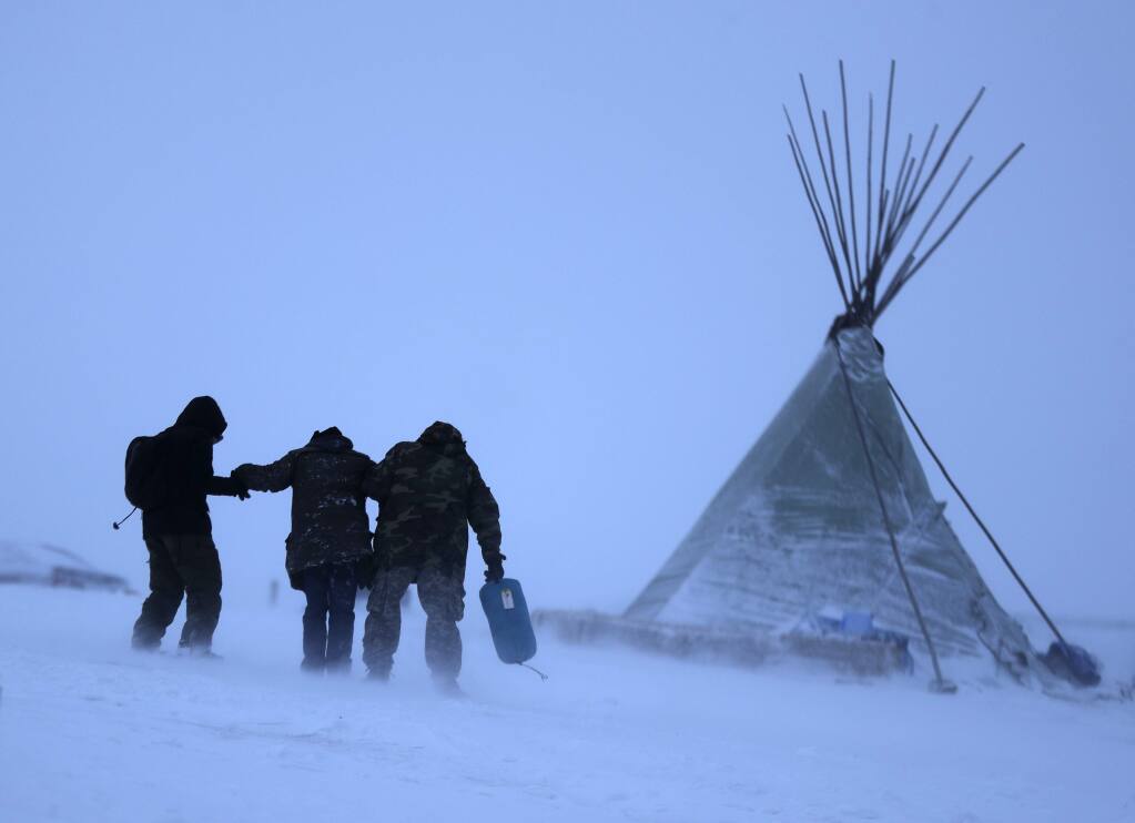 People walk along a snowy hillside in a storm at the Oceti Sakowin camp where people have gathered to protest the Dakota Access oil pipeline in Cannon Ball, N.D. (DAVID GOLDMAN / Associated Press)