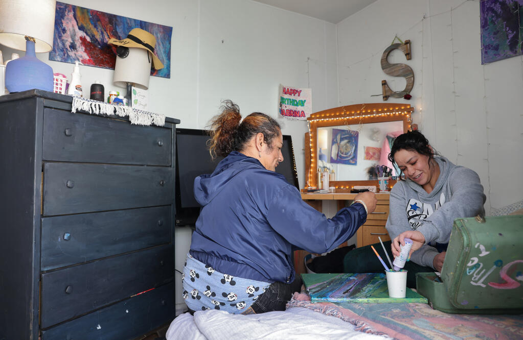 Sabrina Jones, right, teaches Leonel Paniagua how to paint in her housing unit at the Labath Landing Emergency Interim Housing site in Rohnert Park on Tuesday, Feb. 21, 2023. (Christopher Chung/The Press Democrat)