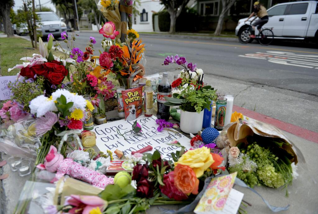 In this Wednesday, May 8, 2019, photo flowers and cards rest on a memorial for Jessica Bingaman, a popular dog walker, who was killed along with five of six dogs she was transporting in Long Beach, Calif. A motorist fleeing police crashed into Bingaman's car on Tuesday. (Brittany Murray/The Orange County Register via AP)