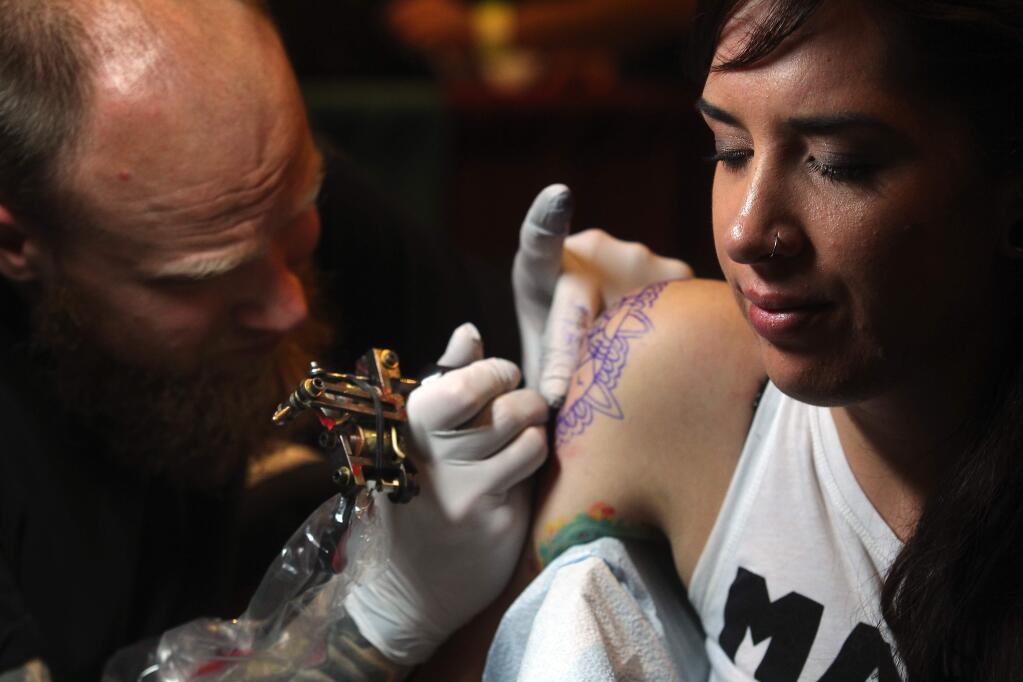 Ian Rydqust of the Guilded Lily Tattoo in Santa Rosa inks Christina Ortega of Ukiah at Izzy's 24th Annual Tattoos and Blues Festival at the Flamingo Hotel. (Photo by John Burgess/The Press Democrat)