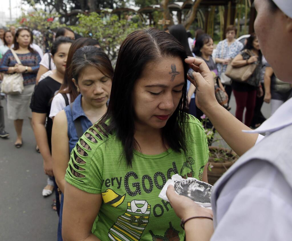A Catholic nun uses an ash to mark with a cross the foreheads of devotees in observance of Ash Wednesday among Roman Catholics at The Redemptorist Church at suburban Paranaque city, south of Manila, Philippines Wednesday, Feb. 18, 2015. Ash Wednesday, which ushers the Season of Lent, is observed to remind people on earth that they are mortals. (AP Photo/Bullit Marquez)