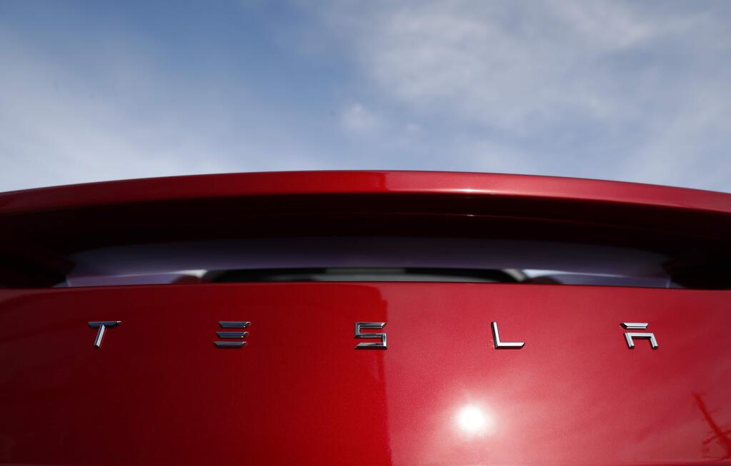 FILE- In this April 15, 2018, file photo the sun shines off the rear deck of a roadster on a Tesla dealer's lot in the south Denver suburb of Littleton, Colo. Electric car maker Tesla Inc. is laying off about 3,600 white-collar workers as it slashes costs in an effort to become profitable. CEO Elon Musk says in an e-mail to workers Tuesday, June 12, that the cuts amount to about 9 percent of the company's workforce of 40,000. (AP Photo/David Zalubowski, File)