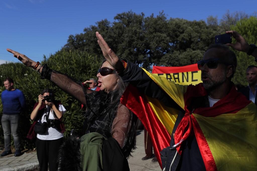 People make the fascist salute as they gather outside Mingorrubio's cemetery, outskirts of Madrid, Thursday, Oct. 24, 2019. Forty-four years after his demise, the remains of Spanish dictator Gen. Francisco are to be dug out of his grandiose resting place outside Madrid and taken to a small family crypt, finally satisfying a long-standing demand of his victims' relatives and others who suffered under his regime. Inscription at ribbons reads in Spanish 'Barcelona always with Franco'. (AP Photo/Manu Fernandez)