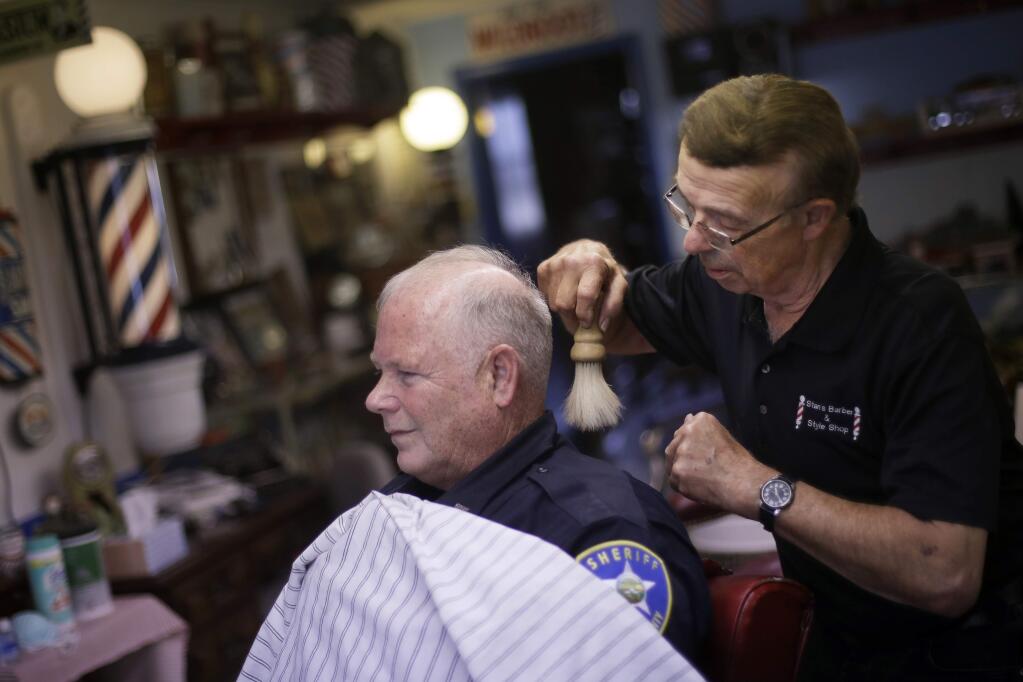 Stan Morin brushes away hair after giving a haircut to Jeff McGee at his barber shop, Thursday, May 21, 2020, in Plainville, Kan. Morin said he has been two to three times busier than normal after reopening a week earlier following a 2-month closure in an effort to stem the spread of the coronavirus. (AP Photo/Charlie Riedel)