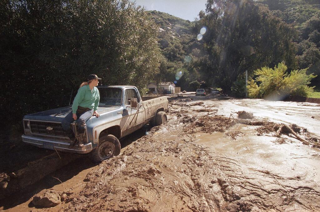 FILE - In this Feb. 24, 1998 file photo, a woman waits for a tow truck on the hood of her brother's pickup after a wall of mud plowed down Laguna Beach Canyon Road in Orange County, Calif. forcing her to evacuate her home, in background. A long anticipated El Nino weather warping is finally here. But for drought-struck California, itís too little, too late, meteorologists say. The National Weather Service Thursday proclaimed the somewhat infamous weather phenomenon El Nino is now in place. Itís a warming of a certain patch of the central Pacific that changes weather patterns worldwide, associated with flooding in some places, droughts elsewhere, a generally warmer globe, and fewer Atlantic hurricanes. El Ninos are usually so important that economists even track it because of how it affects commodities. This year's El Nino that has arrived isnít big and is late so itís unlikely to do much to alleviate the current California drought. (AP Photo/Nick Ut, File)
