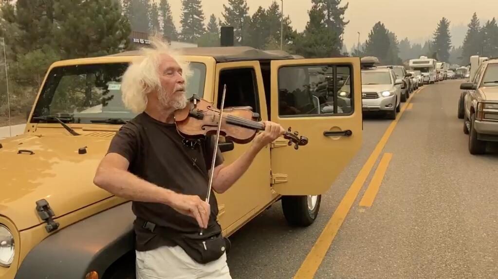 Mel Smothers of South Lake Tahoe plays violin to pass the time as traffic heading east on Highway 50 from South Lake Tahoe comes to a standstill. The backup came after authorities evacuated the entire city of South Lake Tahoe on Monday, Aug. 30, 2021 as the Caldor fire continued its march toward the lake. (Kent Porter / Press Democrat)