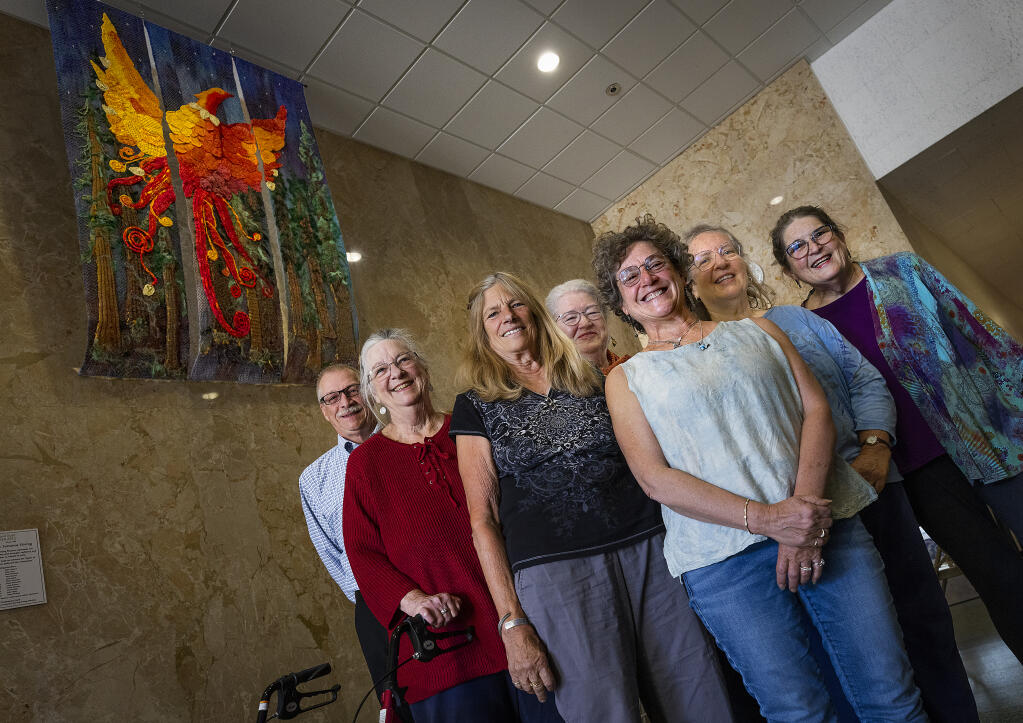 Some of the 25 members of the Redwood Guild of Fiber Arts who created the triptych “Phoenix Rising: Sonoma Strong" at the unveiling of the piece at the Sonoma County Administration building, Monday, Oct. 18, 2022.  (John Burgess/The Press Democrat)