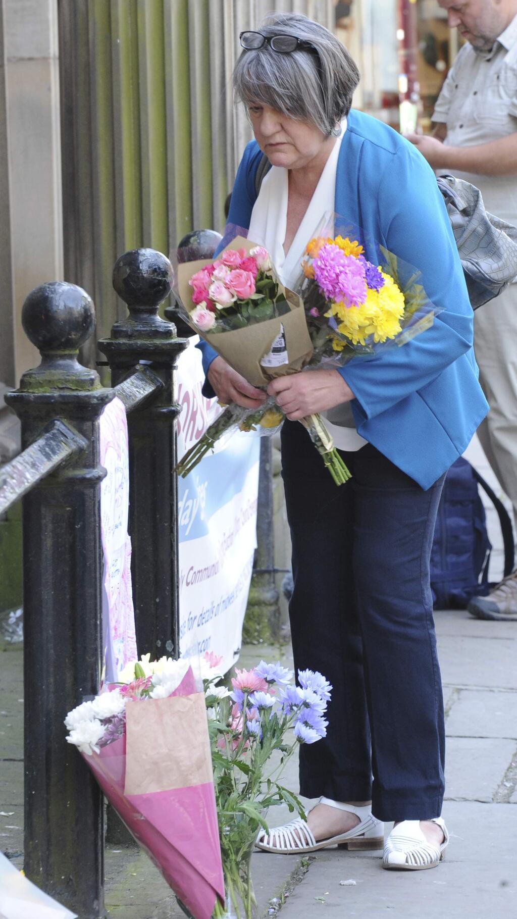 An unidentified member of the public places a floral tribute at St Ann's square, Manchester, England Tuesday May 23, 2017. The Islamic State group claimed responsibility Tuesday for the suicide attack at an Ariana Grande show that left more than 20 people dead as young concertgoers fled, some still wearing the American pop star's trademark kitten ears and holding pink balloons. (AP Photo/Rui Vieira)