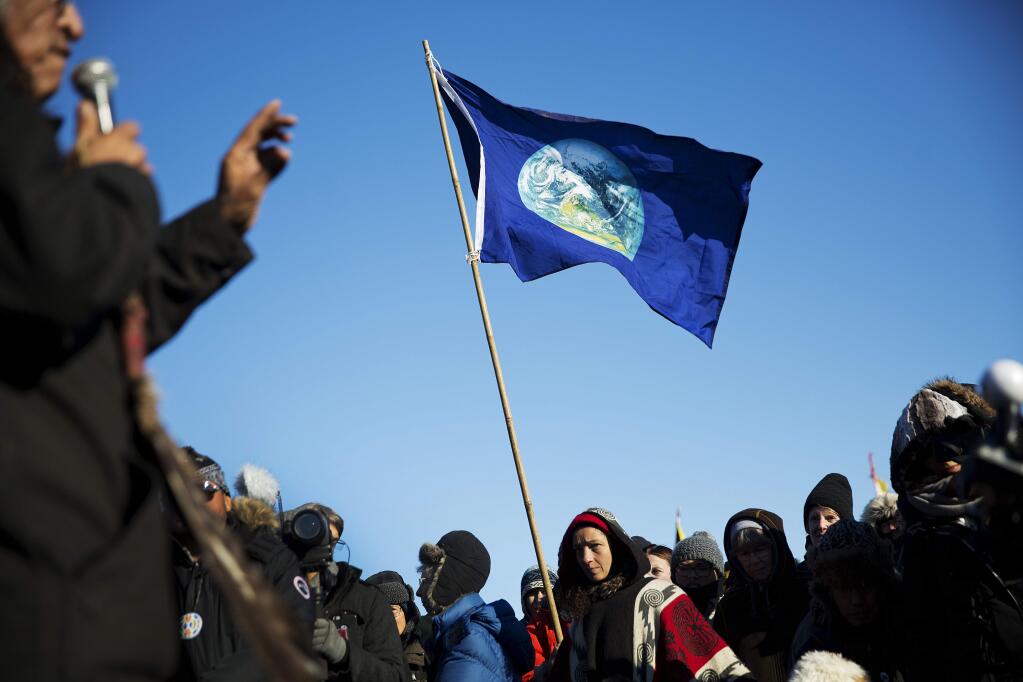 A flag showing planet earth flies above a crowd listening to David Swallow, an Oglala Native American, speak during an interfaith ceremony at the Oceti Sakowin camp where people have gathered to protest the Dakota Access oil pipeline in Cannon Ball, N.D., Sunday, Dec. 4, 2016. (AP Photo/David Goldman)