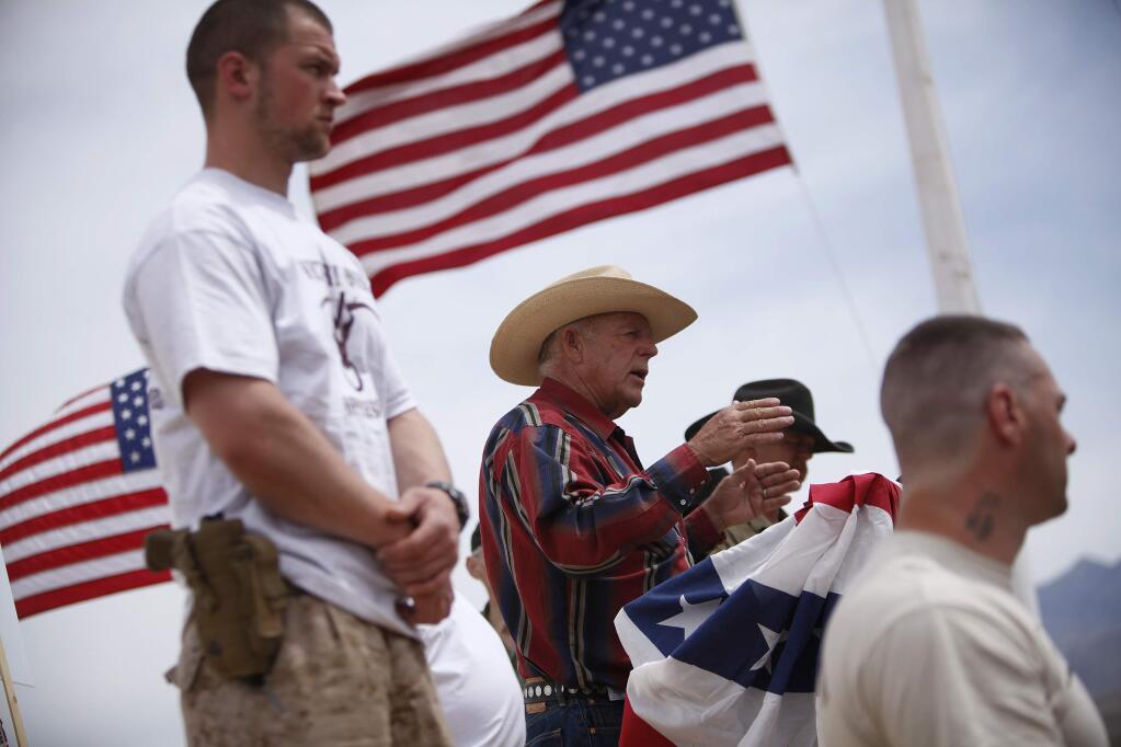 FILE - In this April 18, 2014, file photo, rancher Cliven Bundy, flanked by armed supporters, speaks at a protest camp near Bunkerville, Nev. Gregory Burleson, 53, of Phoenix, was sentenced Wednesday, July 26, 2017, in Las Vegas, Nev., to more than 68 years in federal prison for his role as a gunman in a standoff that stopped federal agents from rounding up cattle near Cliven Bundy's Nevada ranch in 2014. (John Locher/Las Vegas Review-Journal via AP, File)