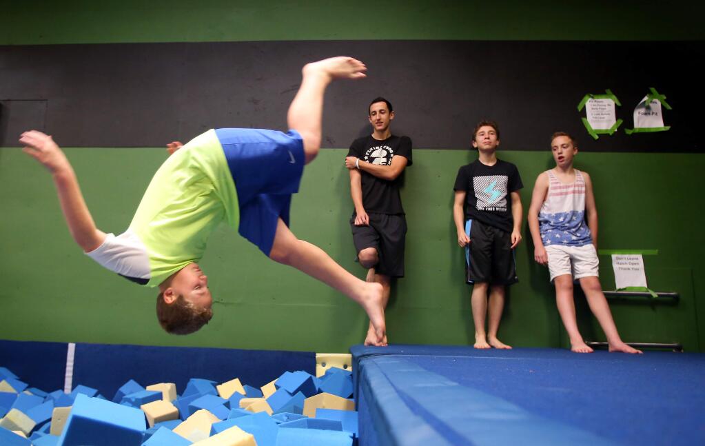 Shay Ledger, left, flips into a foam pit, while instructor Shane Sperling watches, and Teo Goodbuerg, 13, and Keegan Ledger, 13, wait their turn during a winter camp at Flying Frog Academy, in Rohnert Park on Monday, December 22, 2014. (Christopher Chung/ The Press Democrat)