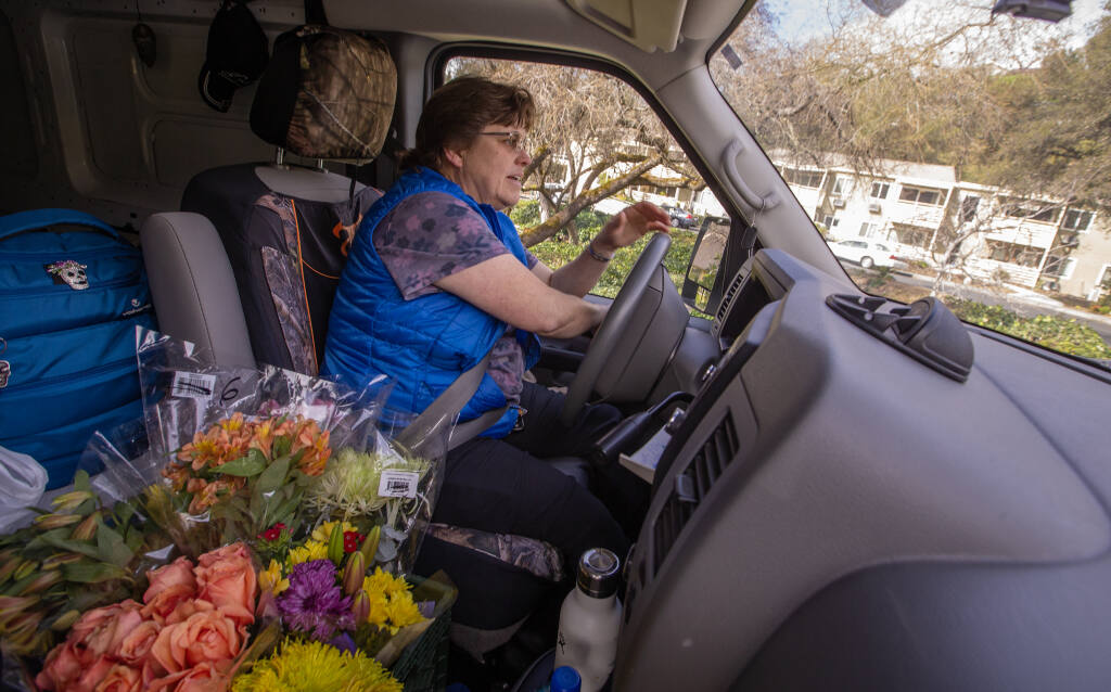 Longtime Council on Aging Meals on Wheels driver and Fleet Manager Shannon Holck drives to her next delivery stop with a passenger seat full of flowers after handing off meals at the Drive Up/Pick Up site in front of the senior center at King's Valley Senior Apartments in Cloverdale, Feb. 21, 2023. (Chad Surmick / The Press Democrat)