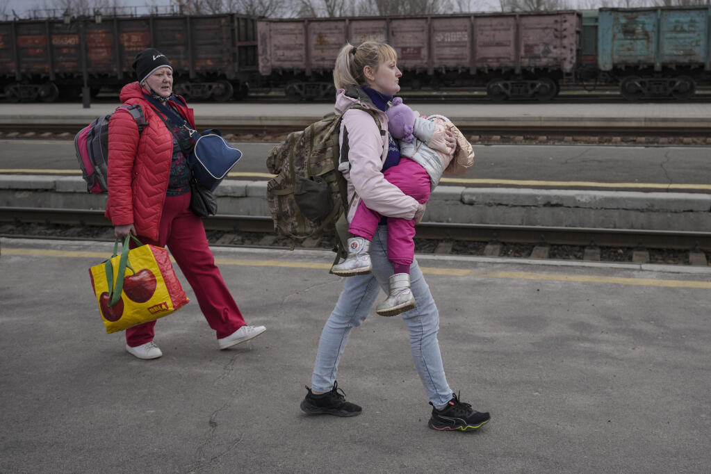 A woman carries a child while walking on a platform to board a Kyiv-bound train in Kostiantynivka, the Donetsk region, eastern Ukraine, Thursday, Feb. 24, 2022. Russia launched a wide-ranging attack on Ukraine on Thursday, hitting cities and bases with airstrikes or shelling, as civilians piled into trains and cars to flee. Ukraine's government said Russian tanks and troops rolled across the border in a “full-scale war” that could rewrite the geopolitical order and whose fallout already reverberated around the world. (AP Photo/Vadim Ghirda)