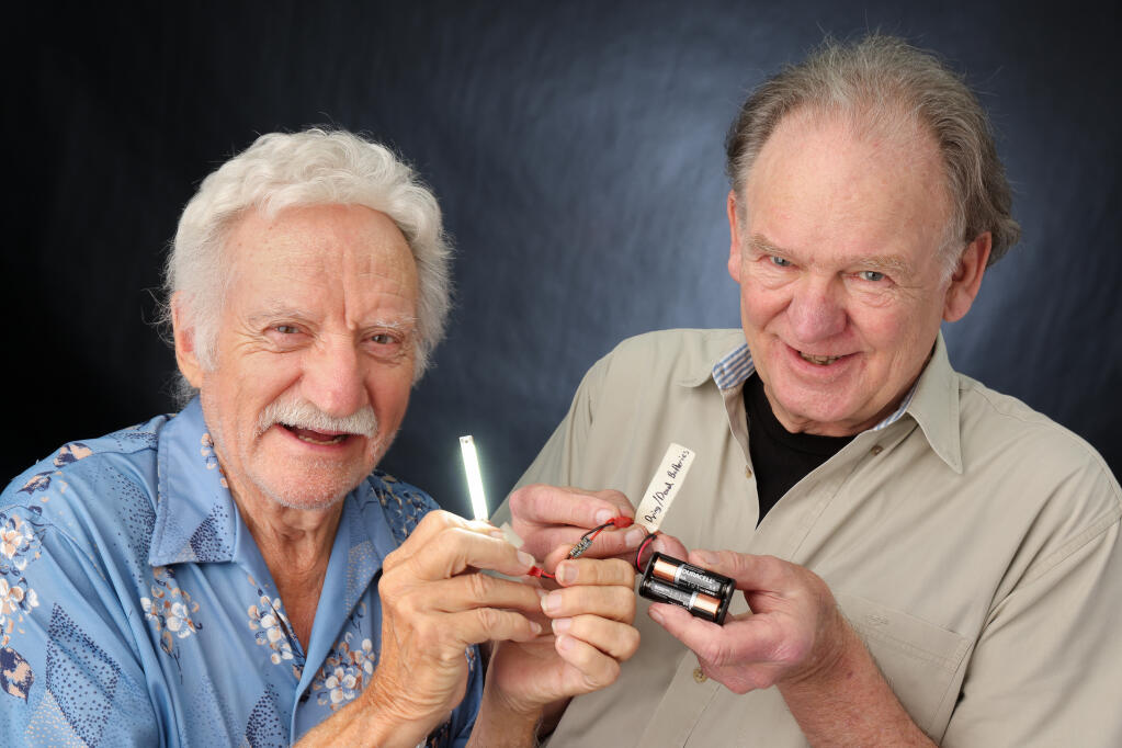 Larry Udell, left, and Bill Seidel demonstrate how the BatterySavers device extends the life of otherwise dying or dead batteries, in Santa Rosa on Tuesday, August 16, 2022. They hope the device will help curb the number of batteries thrown away each year, or can be used to extend the charge of cellphone batteries. (Christopher Chung/The Press Democrat)
