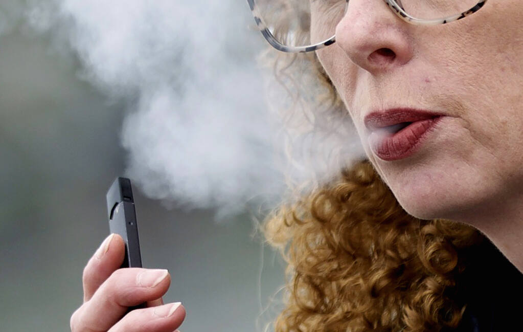 FILE — A woman exhales while vaping from a Juul pen e-cigarette in Vancouver, Wash., April 16, 2019. Juul has asked a federal court, Friday, June 24, 2022, to block a government order to stop selling its electronic cigarettes. Federal health officials on Thursday, June 23,  ordered Juul to pull its electronic cigarettes from the U.S. market, the latest blow to the embattled company widely blamed for sparking a national surge in teen vaping.  (AP Photo/Craig Mitchelldyer, File)