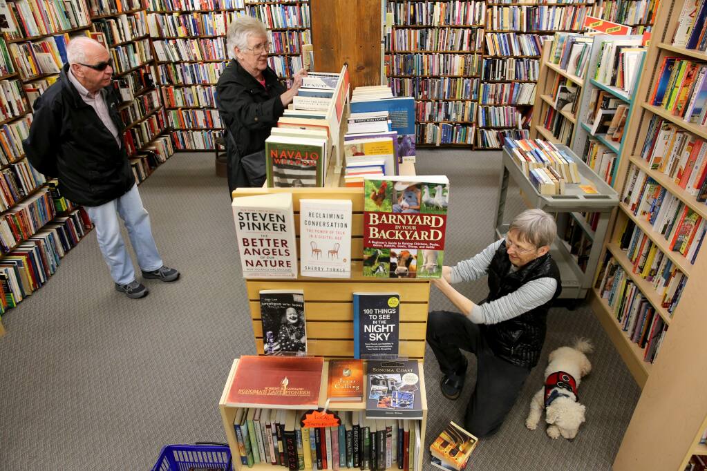 Owner Jill Brown, accompanied by her dog, Marvin, restocks books, as customers Dan and Lyn Jacoby browse through the shelves at Paperbacks Unlimited in Santa Rosa on Monday, April 1, 2019. (BETH SCHLANKER/ The Press Democrat)
