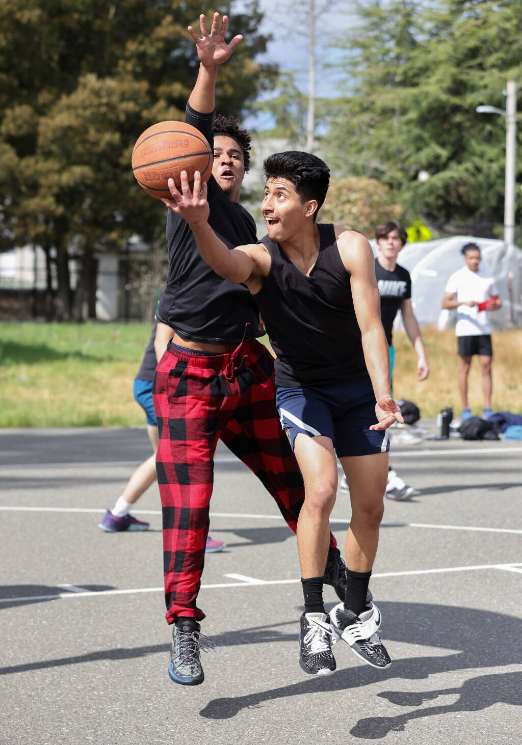 Braulio Juarez, right, scoops a shot around Exodus Daniels during a pickup game of basketball in Sebastopol on Friday, March 25, 2022.  (Christopher Chung/ The Press Democrat)