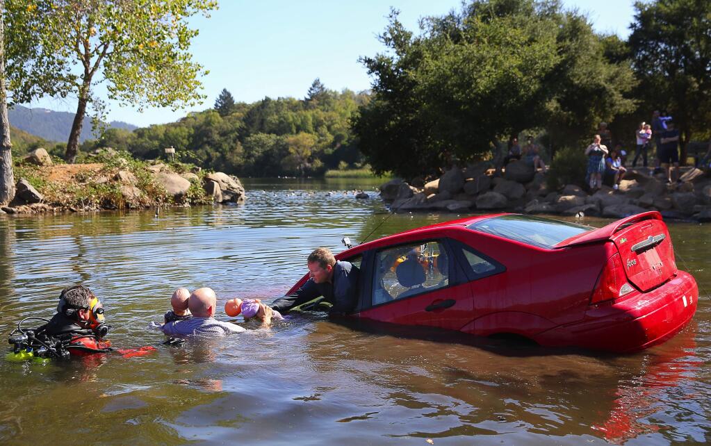 Vehicle passenger Bill Bullard, right, hands two child-sized mannequins to driver Andy Brennan, as they escape a submerged vehicle during a demonstration, while diver Jim Eckhoff stands by, during a demonstration at Lake Ralphine, in Santa Rosa, on Monday, September 26, 2016. All three people are members of the Sonoma County Sheriff's Department volunteer dive team.(Christopher Chung/ The Press Democrat)