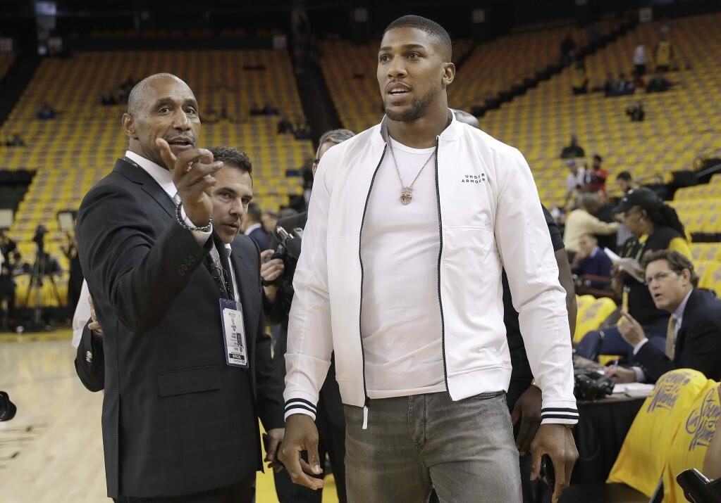 FILE - In this May 2, 2018, file photo, Golden State Warriors director of team security Ralph Walker, left, gestures next to boxer Anthony Joshua before Game 4 of the NBA basketball Western Conference Finals between the Warriors and the Houston Rockets in Oakland, Calif. Walker, who in recent seasons had primarily worked closely with Stephen Curry, has departed the organization to spend more time with family. Walker confirmed his exit via text message, saying, “Will miss you all.” He had been a fixture on the Golden State sidelines and almost anywhere Curry went, staying close to the two-time MVP at home and on the road. Walker is a former member of the Oakland Police Department. (AP Photo/Marcio Jose Sanchez, File)