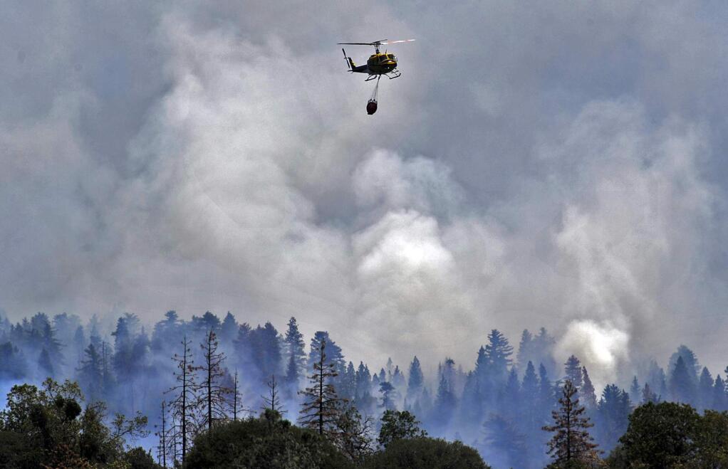 A helicopter flies away from a burning ridge after dropping water on the Willow Fire near Bass Lake, Calif., Monday, July 27, 2015. (Eric Paul Zamora / Fresno Bee)