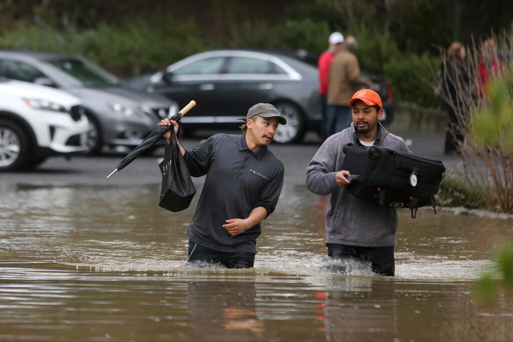 Farmhouse Inn employees Brayan Velazquez, left, and Alex Lopez help the guests with their luggage as they walk through the floodwaters at the entrance on River Road in Forestville on Wednesday, Feb. 27, 2019. (BETH SCHLANKER/ PD)