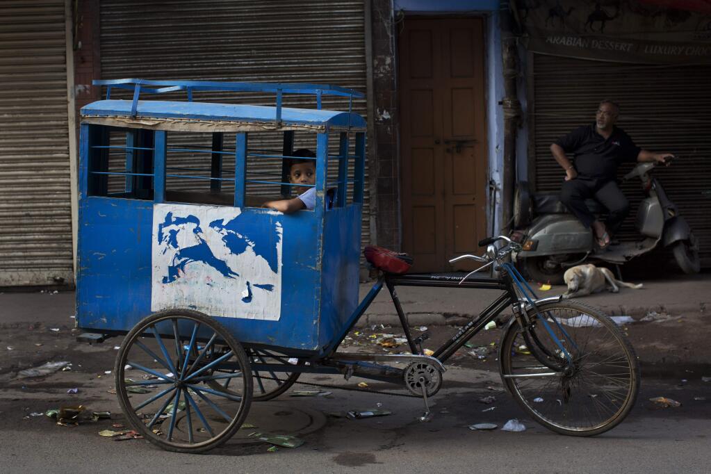 An Indian child on his way to school sits inside a custom-made cycle rickshaw as he awaits other children to join him in New Delhi, India, Wednesday, July 22, 2015. (AP Photo/Bernat Armangue)