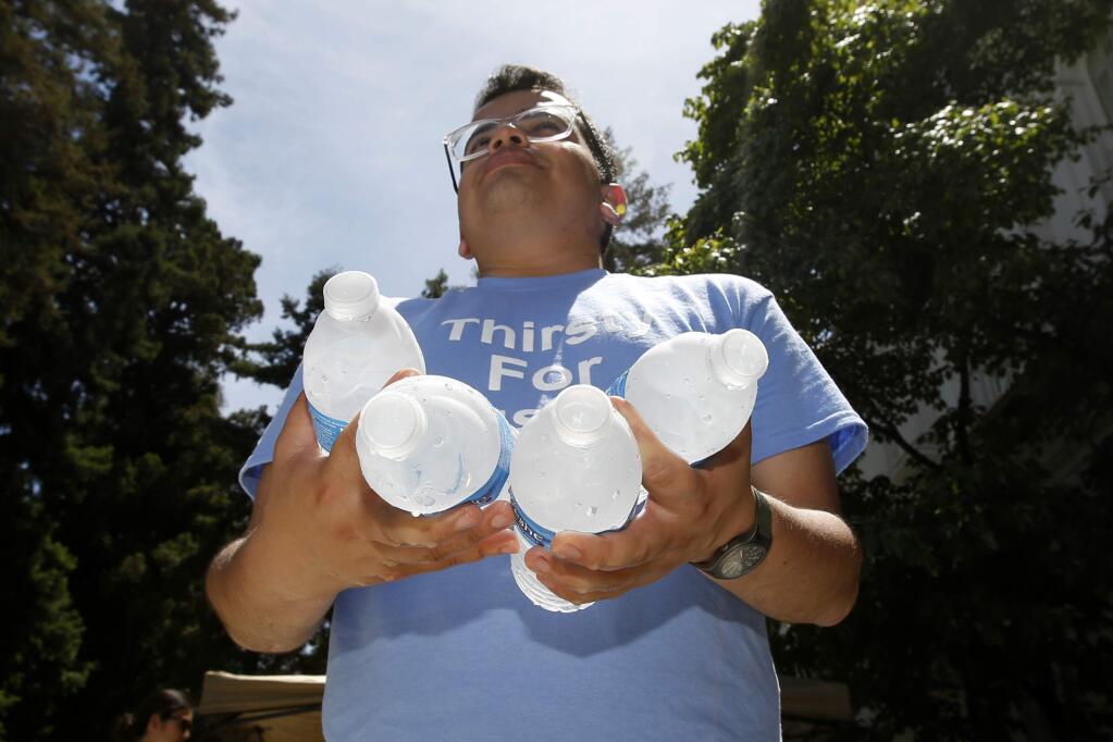 Cesar Garcia Lopez holds bottles of water to be passed out at a rally in support of a clean water measure before the legislature, in Sacramento, Calif., Monday June 10, 2019. The California legislative leaders have agreed to $130 million a year to make improvements in communities where people still can't drink the water from their taps.(AP Photo/Rich Pedroncelli)