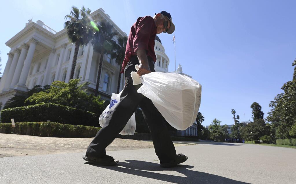 FILE - In this Aug. 12, 2014 file photo, a man carries plastic single-use bags past the State Capitol in Sacramento, Calif. Election officials said Monday, Feb. 23, 201 that a trade group had turned in enough signatures to qualify a referendum on Californiaís plastic bag ban law, suspending implementation of the nationís first statewide ban until voters weigh in on the November 2016 ballot. (AP Photo/Rich Pedroncelli, File)