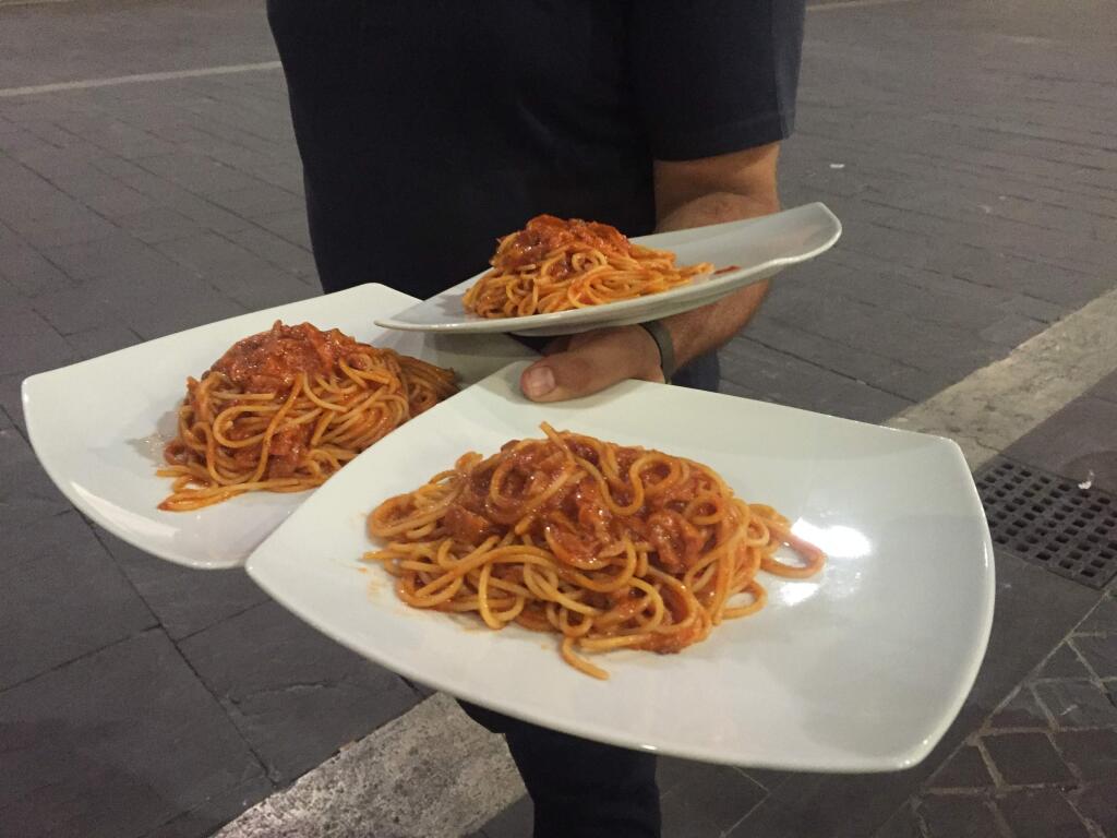 Waiter Andrea Orsini serves pasta all'amatriciana at a restaurant in Ascoli Piceno, Italy, Friday, Aug. 26, 2016. Food lovers and chefs in Italy and beyond are urging restaurants to serve up more pasta all'amatriciana in a move to support the quake-hit hometown of the hearty dish. The rustic food, made of tomato sauce with pork jowl and topped with pecorino cheese, comes from Amatrice, which was destroyed by this week's earthquake and the idea is for some of the proceeds to go to help the devastated areas rebuild. (AP Photo/Gregorio Borgia)