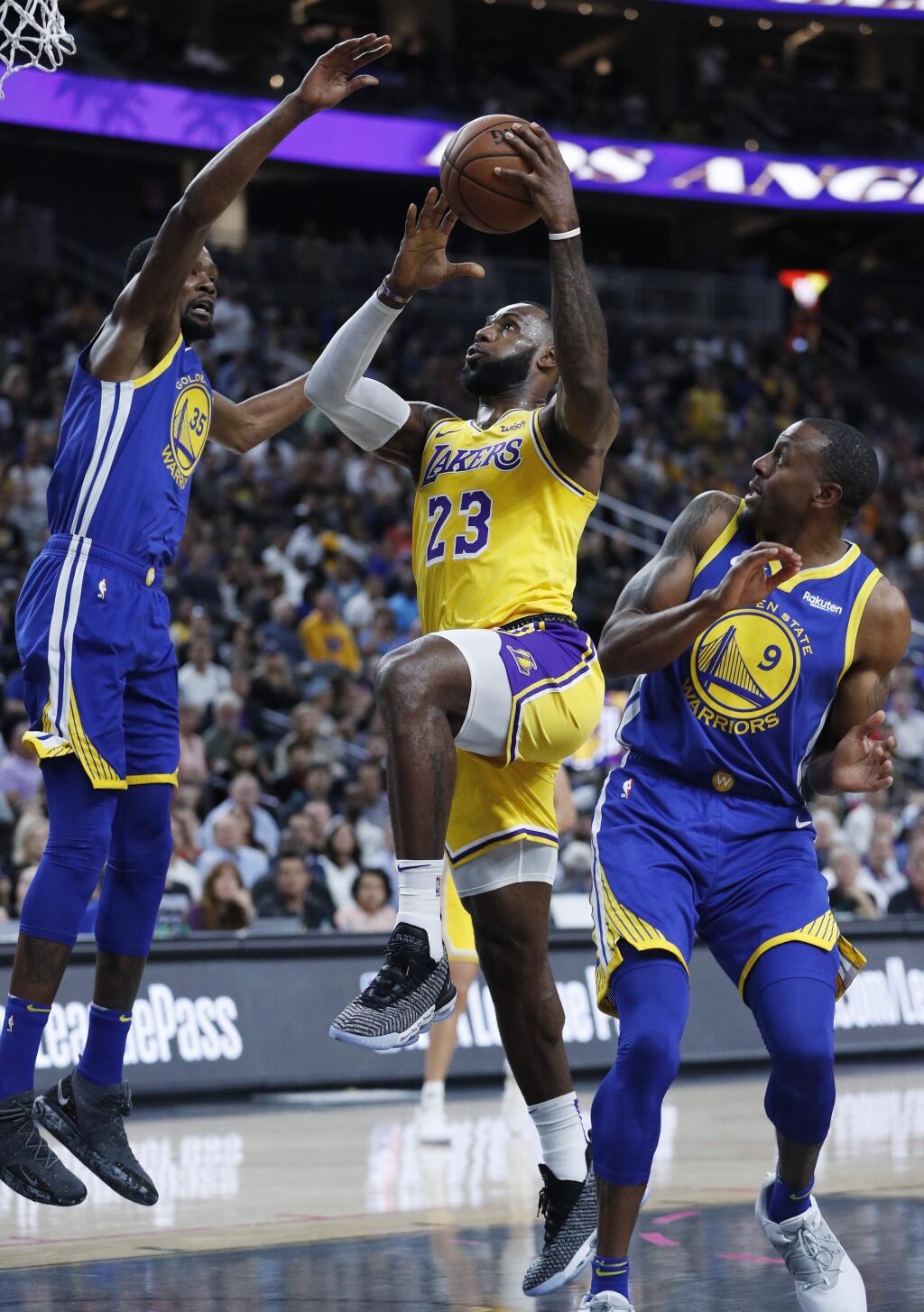 Los Angeles Lakers forward LeBron James (23) shoots between Golden State Warriors forward Kevin Durant, left, and guard Andre Iguodala during the first half of an NBA preseason basketball game Wednesday, Oct. 10, 2018, in Las Vegas. (AP Photo/John Locher)