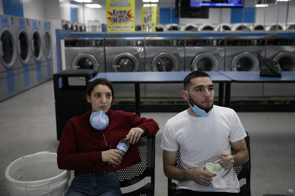 A couple watches TV while doing their laundry amid the coronavirus pandemic in the Vermont Square neighborhood of Los Angeles, Thursday, May 21, 2020. While most of California took another step forward to partly reopen in time for Memorial Day weekend, Los Angeles County didn't join the party because the number of coronavirus cases has grown at a pace that leaves it unable to meet even the new, relaxed state standards for allowing additional businesses and recreational activities. (AP Photo/Jae C. Hong)