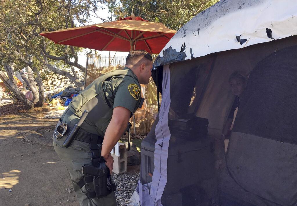 An Orange County sheriff's deputy calls to residents inside a tent in Anaheim, Calif., Monday, Jan. 22, 2018, to let them know they'll need to leave the area and that the county will assist with the move if they need. Southern California authorities on Monday went tent to tent telling the homeless they're shutting down the large riverbed encampment some have called home for years. (AP Photo/Amy Taxin)
