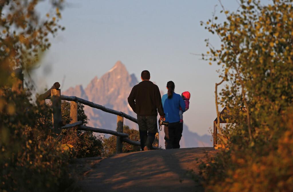 FILE - In this Aug 25, 2016 file photo, on the 100th anniversary of the National Park Service, visitors stroll with their baby as the sun at dawn illuminates mountain peaks as seen from Signal Mountain in Grand Teton National Park, Wyo. Visitation to America's national parks has set new records for three consecutive years. (AP Photo/Brennan Linsley, file)