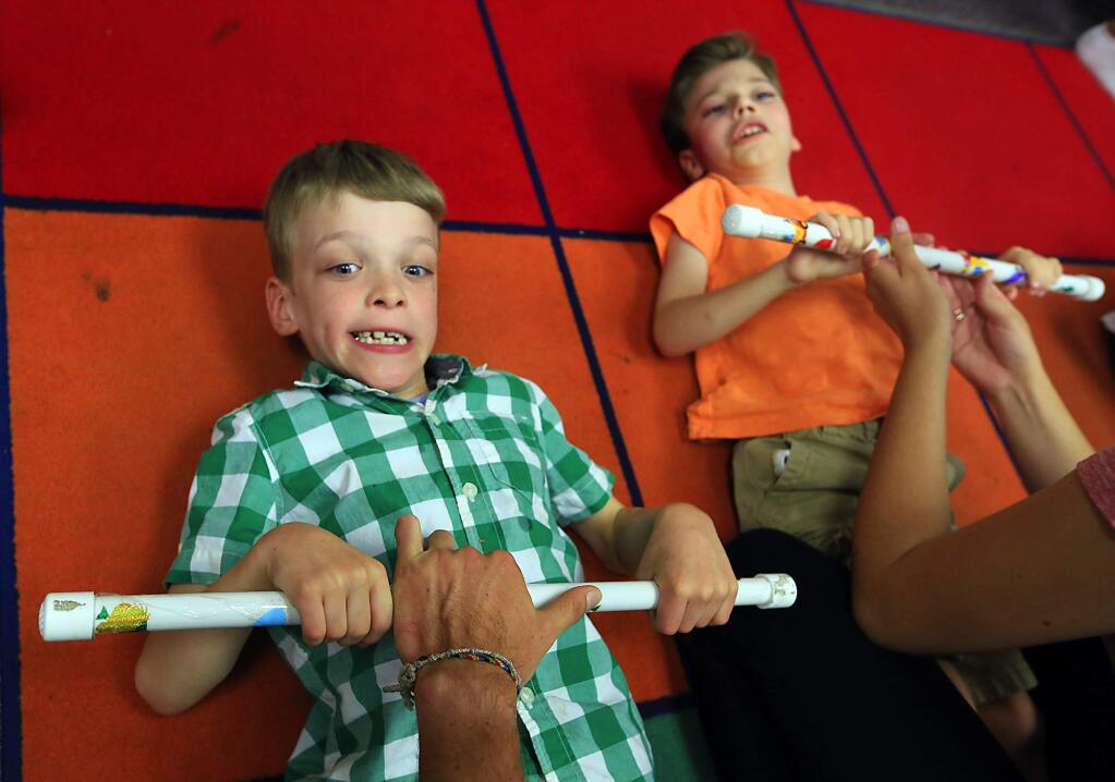 -Above: Nanny Carley Herrera helps Royce Avner, 3, put on his braces and shoes.-Left: Drake Becker, 7, left, and Lucas Stisher, 8, work hard at sit-ups.