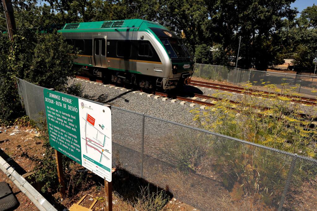 A SMART train passes between the two sides of Jennings Avenue, which does not have a crossing for pedestrian and bicycle traffic, in Santa Rosa, California, on Friday, July 27, 2018. The sign, at left, explains the detour to the nearest rail crossing at Guerneville Road where pedestrians and bicyclists can access the opposite side of Jennings Avenue. (Alvin Jornada / The Press Democrat)