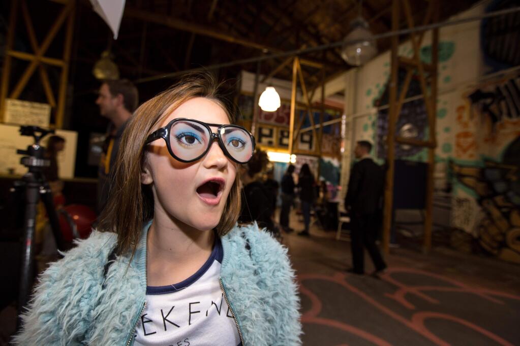 Violet Ross, 8, of Santa Rosa, tries on costume glasses before she poses for a 'green screen' photo provided by Megan Rhodes Photography at the Out There Exposition in Santa Rosa on Sunday, April 29, 2018. (DARRYL BUSH/ FOR THE PD)