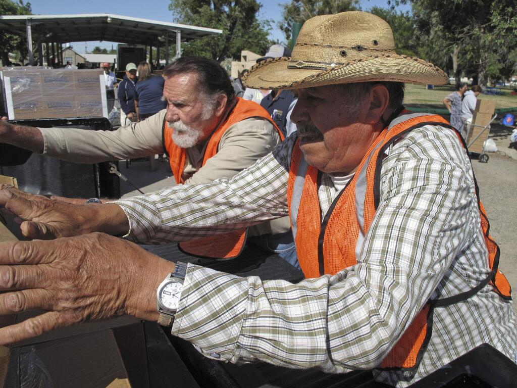 In this June 4, 2015, photo, Fidel Fraga, right, volunteers at a food distribution event in Firebaugh, Calif., serving hundreds of farmworkers out of work because of the states relentless drought. The food is provided through emergency drought relief funds. Fraga also collected his own box of food because has been laid off for months from his job driving a tractor at a Central Valley farm. Although the drought-assistance package has helped communities across California cope with the driest conditions in recent memory, millions of dollars remain untapped more than one year after it was provided, showing how slowly the wheels of government can turn even in a crisis. (AP Photo/Scott Smith)