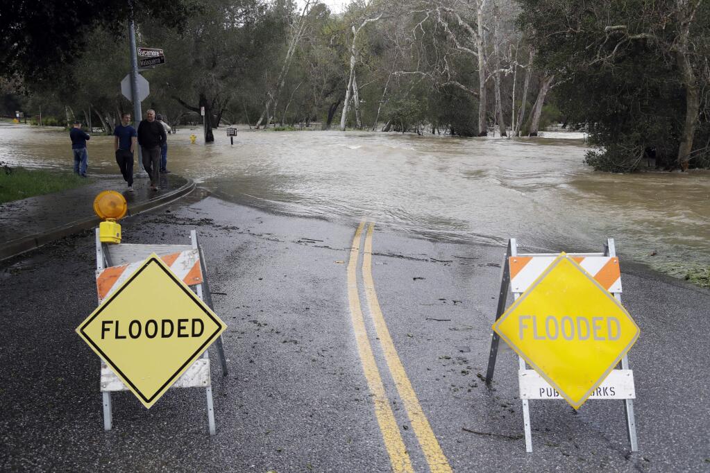 Signs block a road which runs into the overflowing Coyote Creek Tuesday, Feb. 21, 2017, in Morgan Hill, Calif. Rains have saturated once-drought stricken California but have created chaos for residents hit hard by the storms. The latest downpours swelled waterways to flood levels and left about half the state under flood, wind and snow advisories. (AP Photo/Marcio Jose Sanchez)
