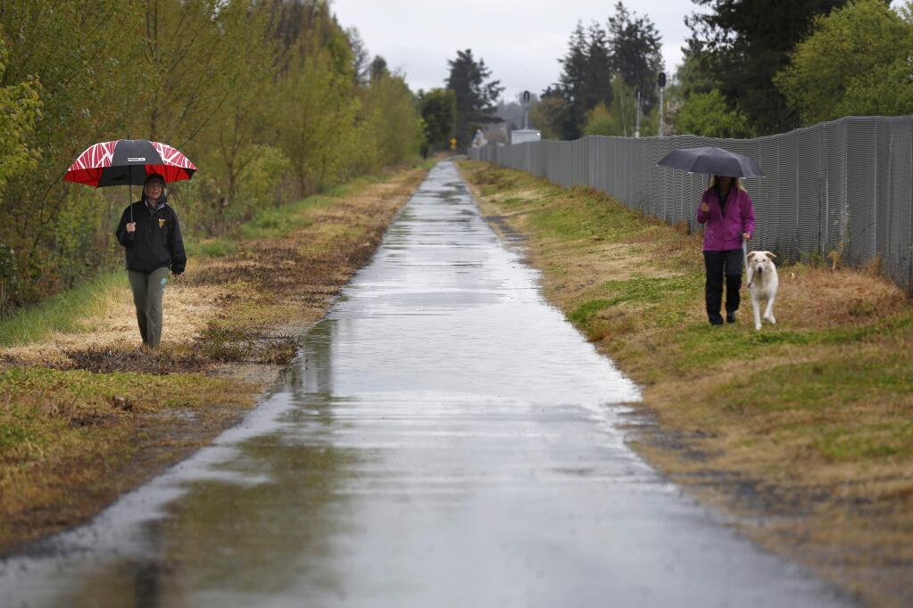 Despite the rain, friends Nadine Finn, left, and Karey Fogle keep their distance from each other while they talk and get some exercise along the SMART pathway in Rohnert Park on Sunday, April 5, 2020. (BETH SCHLANKER/ The Press Democrat)