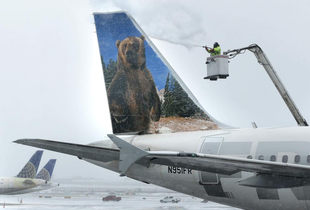 A crewmember de-ices a Frontier Airlines plane at LaGuardia Airport in New York, Monday, Jan. 26, 2015. More than 5,000 flights in and out of East Coast airports have been canceled as a major snowstorm packing up to three feet of snow barrels down on the region. (AP Photo/Seth Wenig)